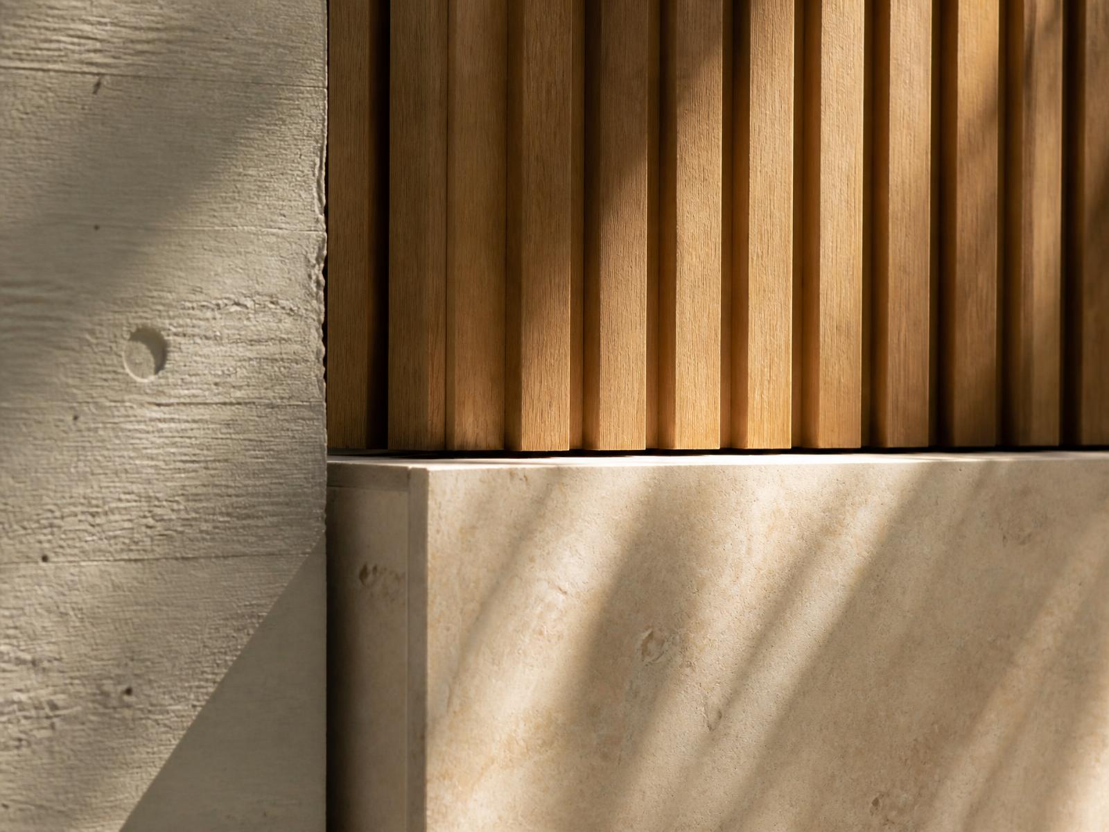 Close-up of board-marked concrete, oak slats and limestone in raking sunlight