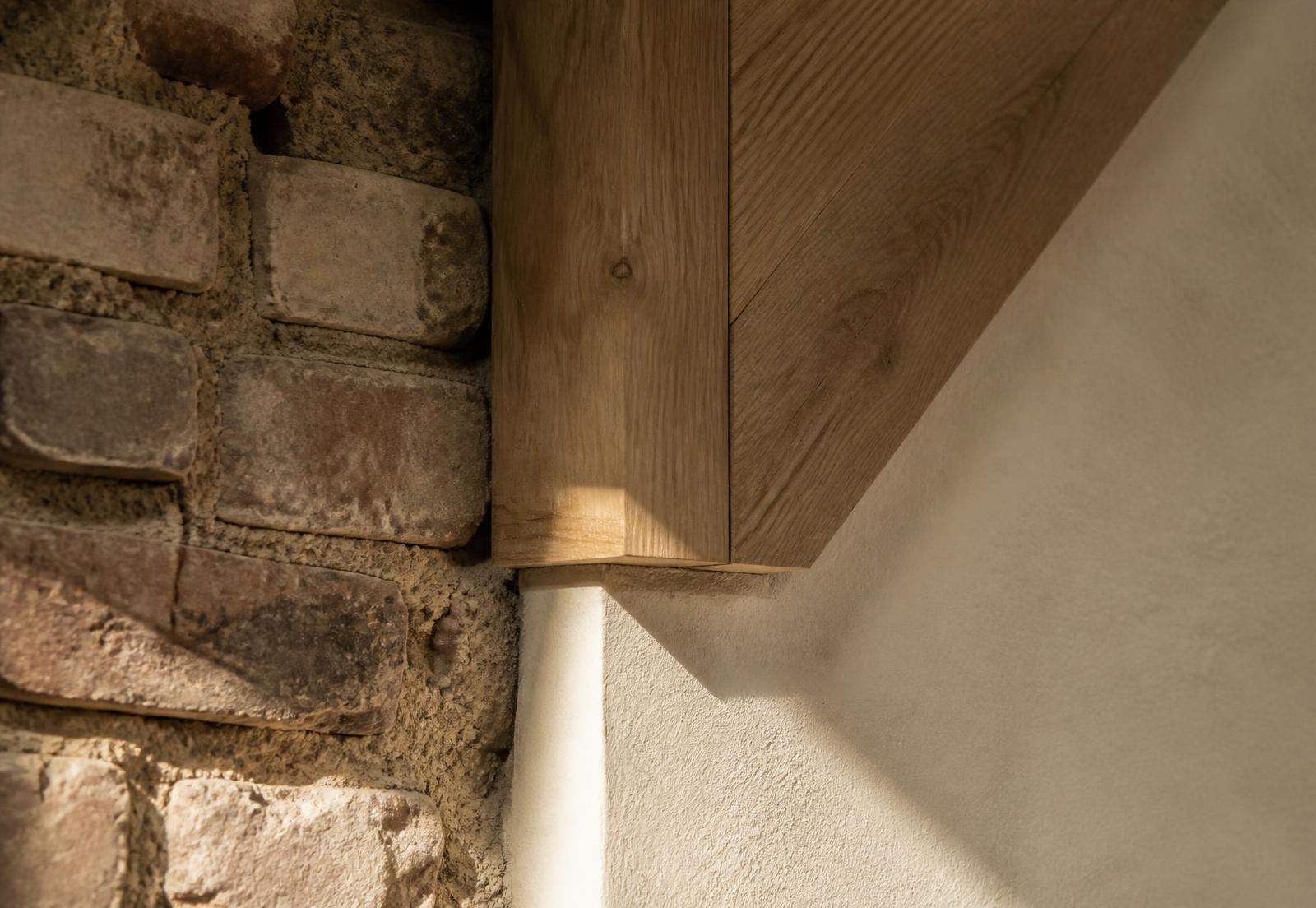 Detail of reclaimed brick meeting new oak joinery and lime plaster in raking daylight